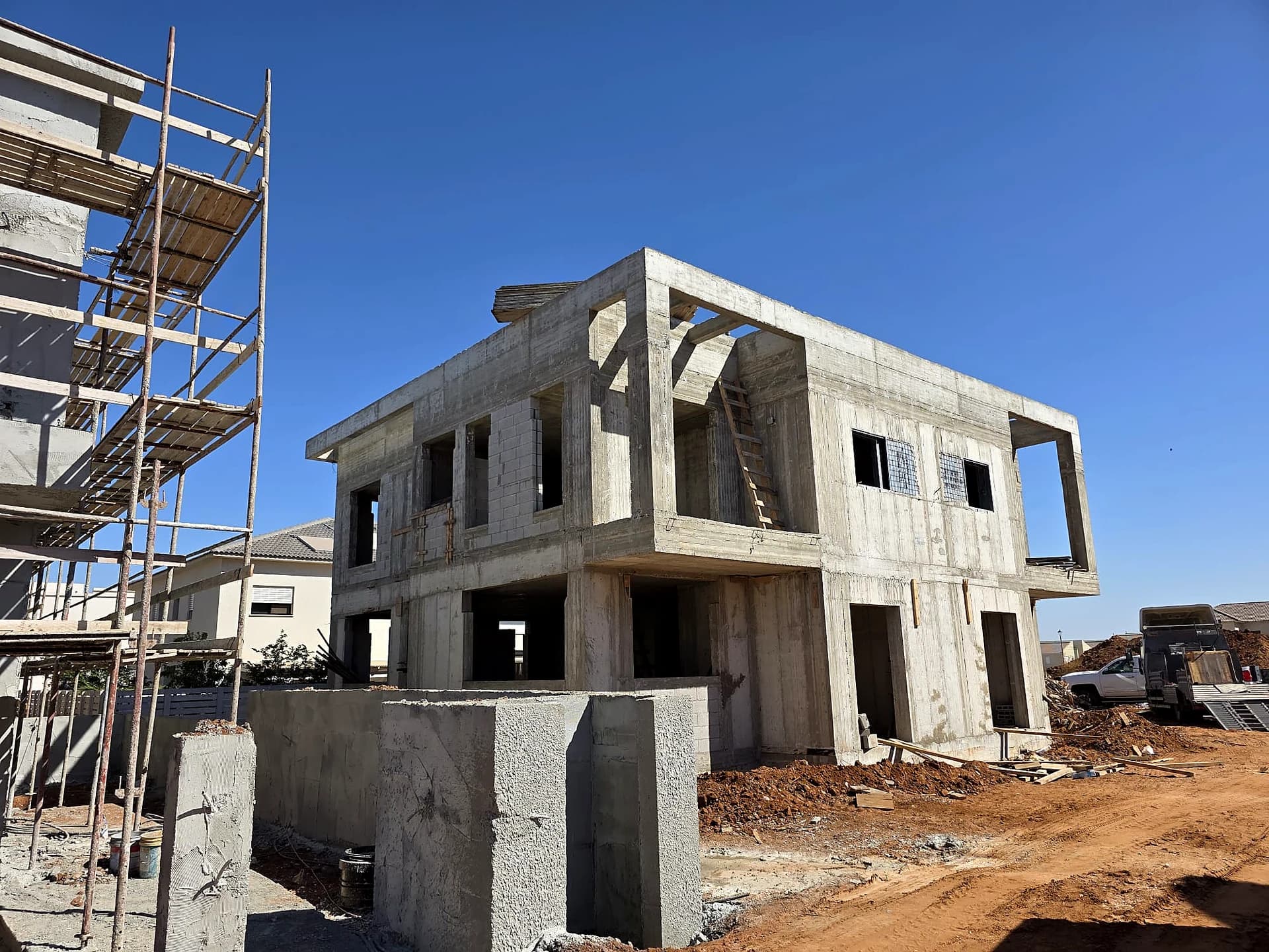 בית פרטי גדול בשלב שלד בטון, 2 קומות עם פרגולת בטון יצוקה על הגג, פיגומים לעיבוד חזיתות