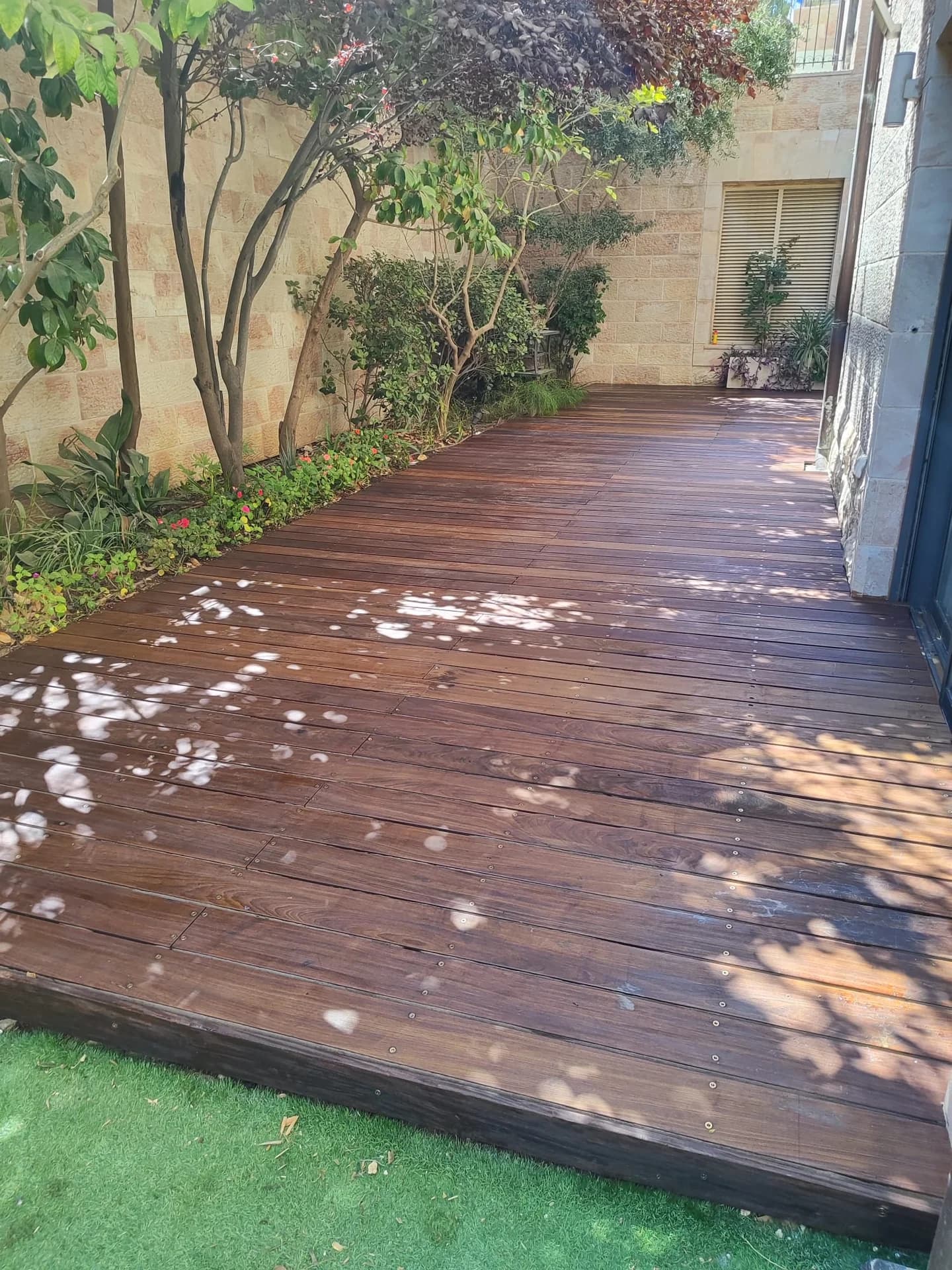 דק עץ איפה בגוון אגוז כהה משמש כשביל גישה לבית פרטי בין צמחייה