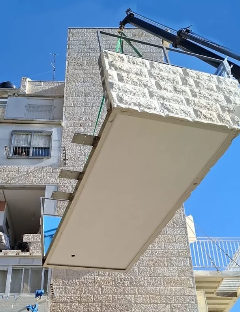 מנוף מרים מרפסת טרומית מחופה אבן ירושלמית ומחבר אותה לדופן בניין מגורים רב-קומות