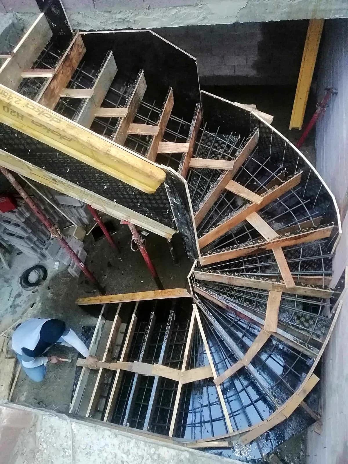 מבט מלמעלה על יציקת מדרגות לולייניות בבטון מזוין, טפסות עץ דוקה צהובות, פועל בתחתית
