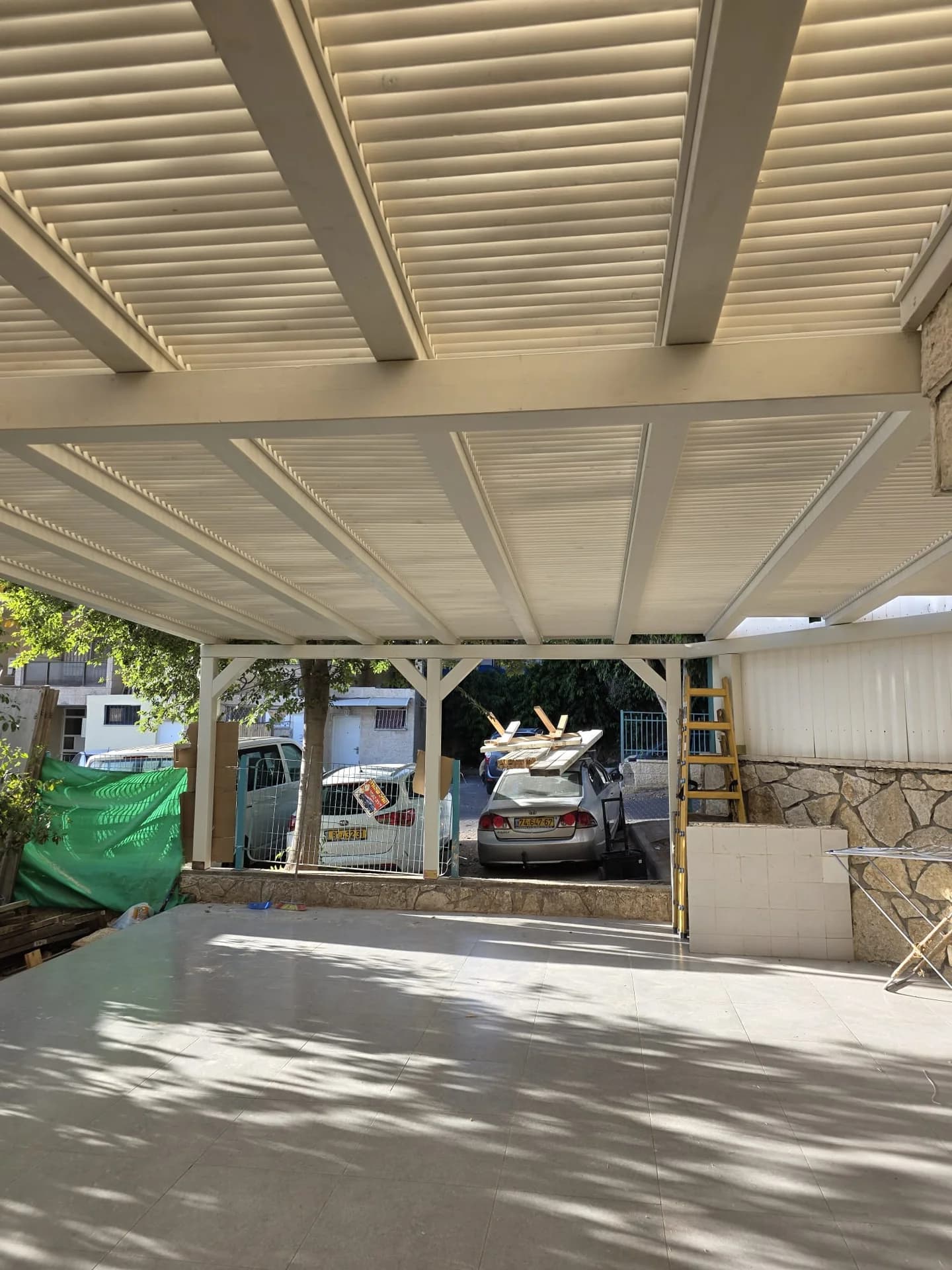 פרגולת אלומיניום לבנה עם רפפות צרות מעל אזור חניה ביתי, צל מקצועי