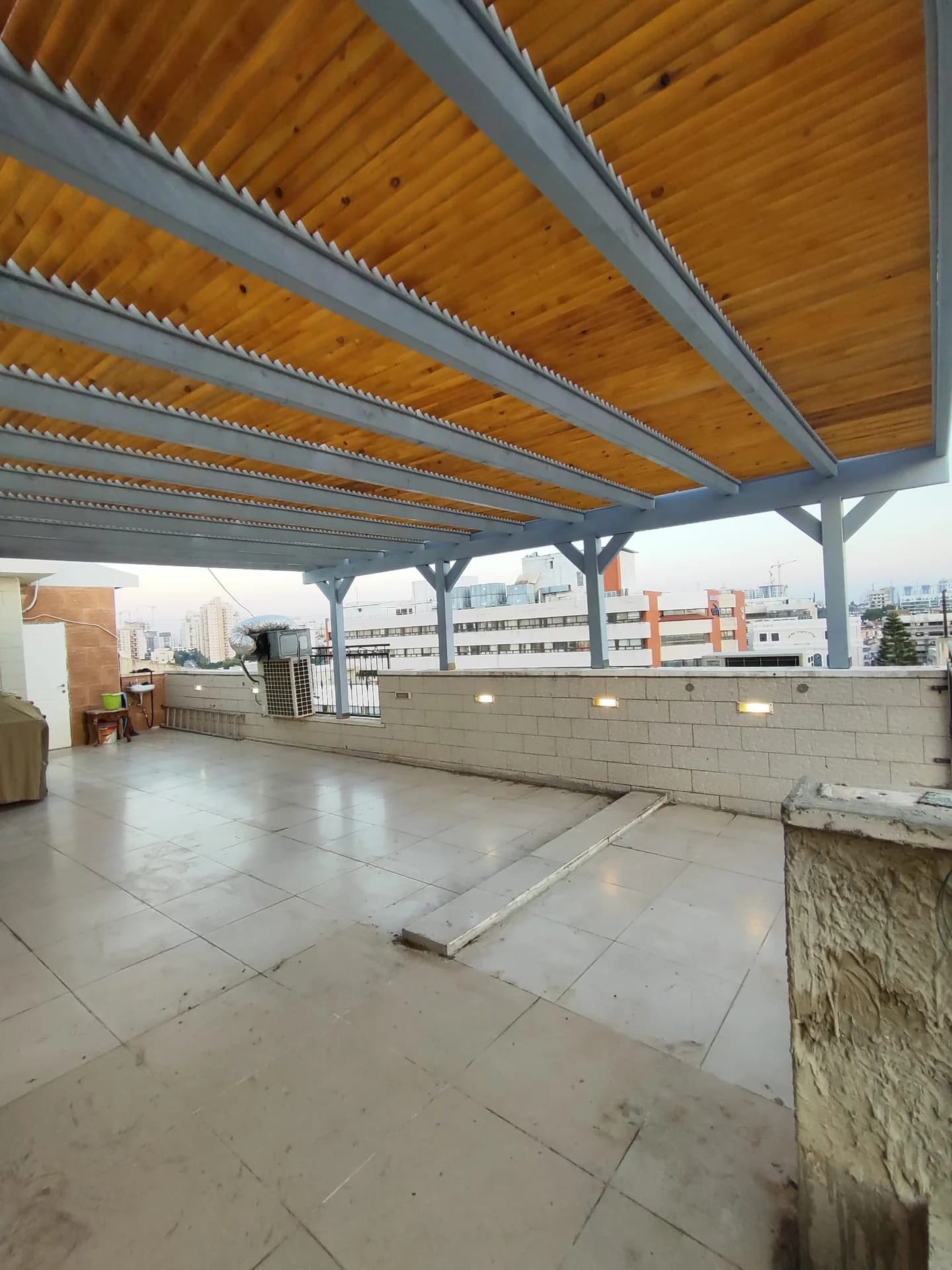 פרגולת היברידית עץ ומתכת אפורה על גג מרפסת, נורות תאורה מוטמעות בקיר