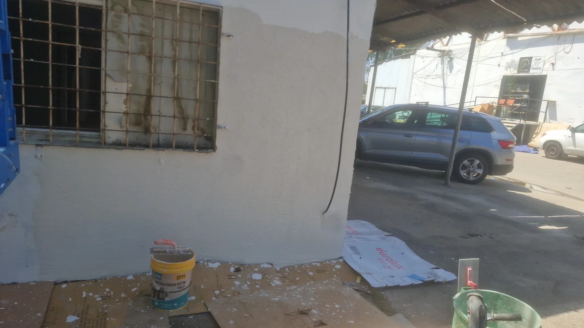 שיפוץ חזית מבנה: קיר חיצוני אחרי טיוח וצביעה לבנה, סורגים על חלון, אזור עבודה מוכן