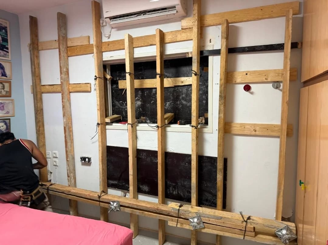 תהליך פירוק קיר בחדר עם פיגום עץ פנימי לתמיכה זמנית, עובד מקצועי