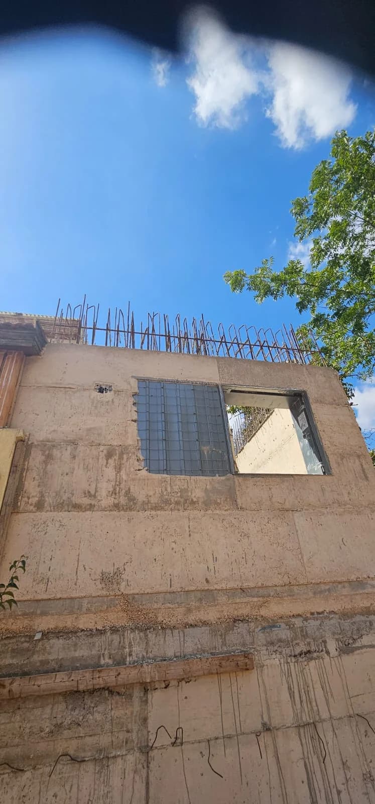 מבט מלמטה על קיר בית קיים עם ברזל זיון בולט מהגג, הכנה לתוספת קומה