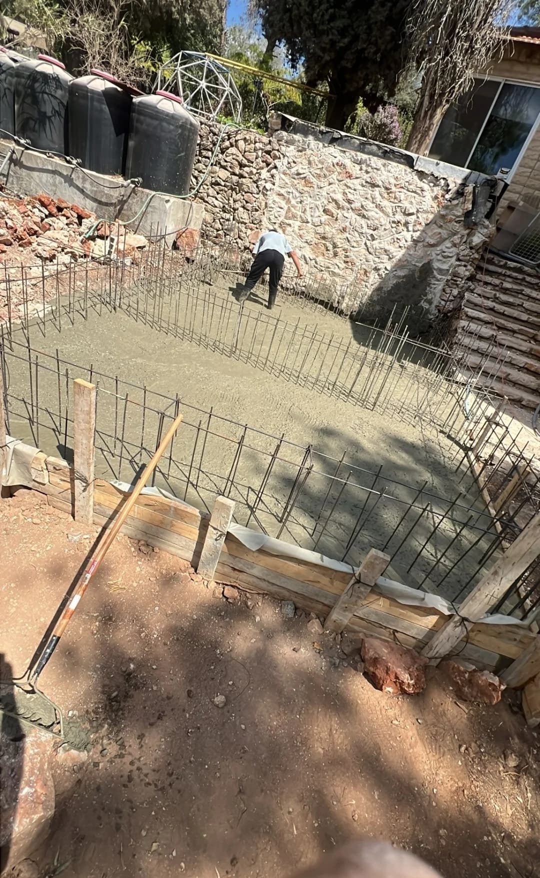 יציקת בטון לרצפת ממ"ד, פועל מקצועי מחליק את הבטון הרטוב, זיון בולט מסביב לקיר